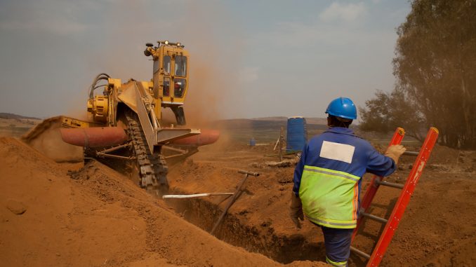 Construction,Worker,Watching,A,Trencher,Machine,Digging,And,Trench,For